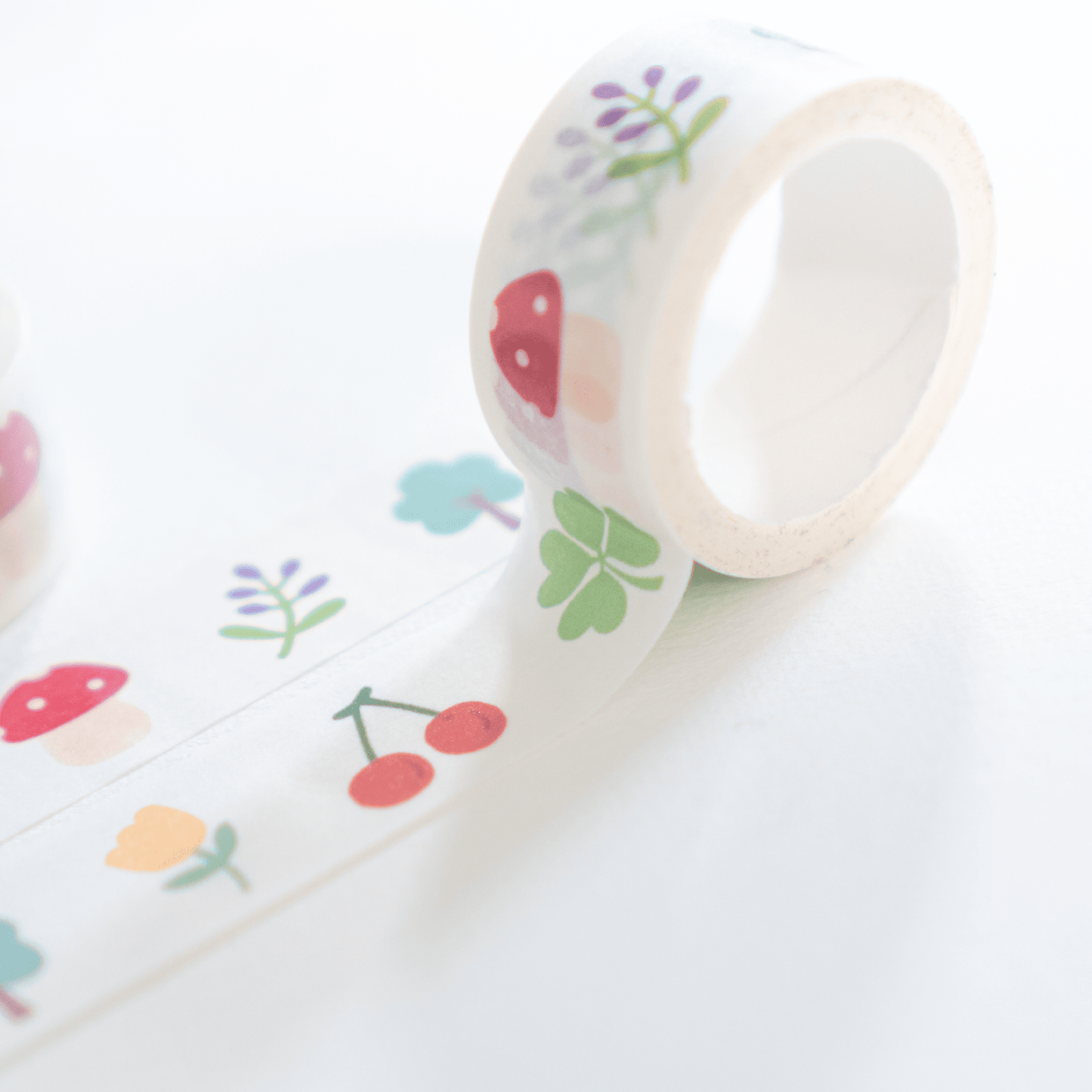 A roll of white washi tape with colorful printed motifs, including red strawberries, green clovers, red cherries, and purple flowers, shown on a clean white background.