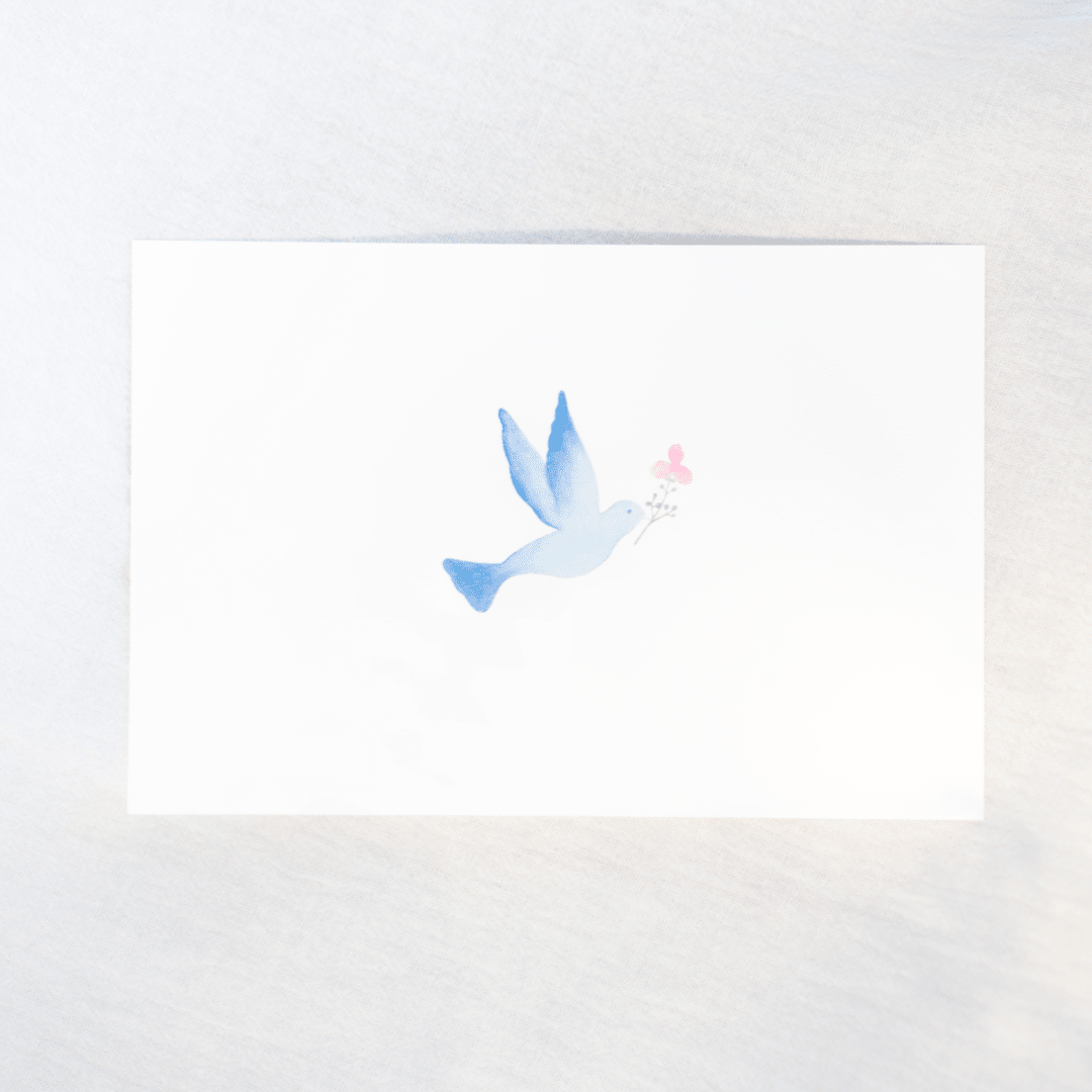 A white rectangular card featuring a delicate watercolor illustration of a blue bird holding a small pink flower, photographed on a light neutral background.