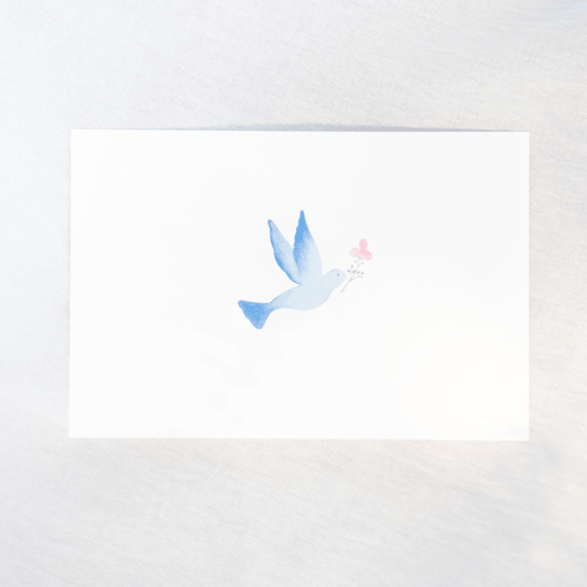 A white rectangular card featuring a delicate watercolor illustration of a blue bird holding a small pink flower, photographed on a light neutral background.