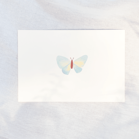 A greeting card featuring a delicate watercolor butterfly with pastel blue and yellow wings and a small brown body, displayed on a soft, light gray textured fabric background.