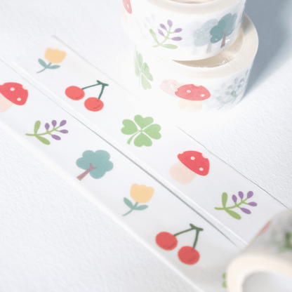 White washi tape with a colorful spring and summer pattern, including cherries, flowers, and mushrooms, shown in rolls and a flat strip on a white background.